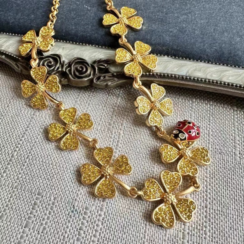 Gold clover crystal necklace with ladybug accent charm, layered on fabric
