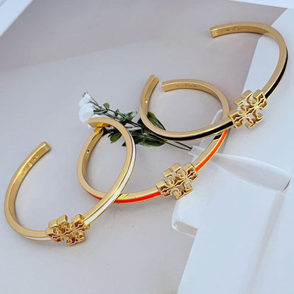 Open gold-tone bangle with cutout logo charm and orange enamel edge stripe
