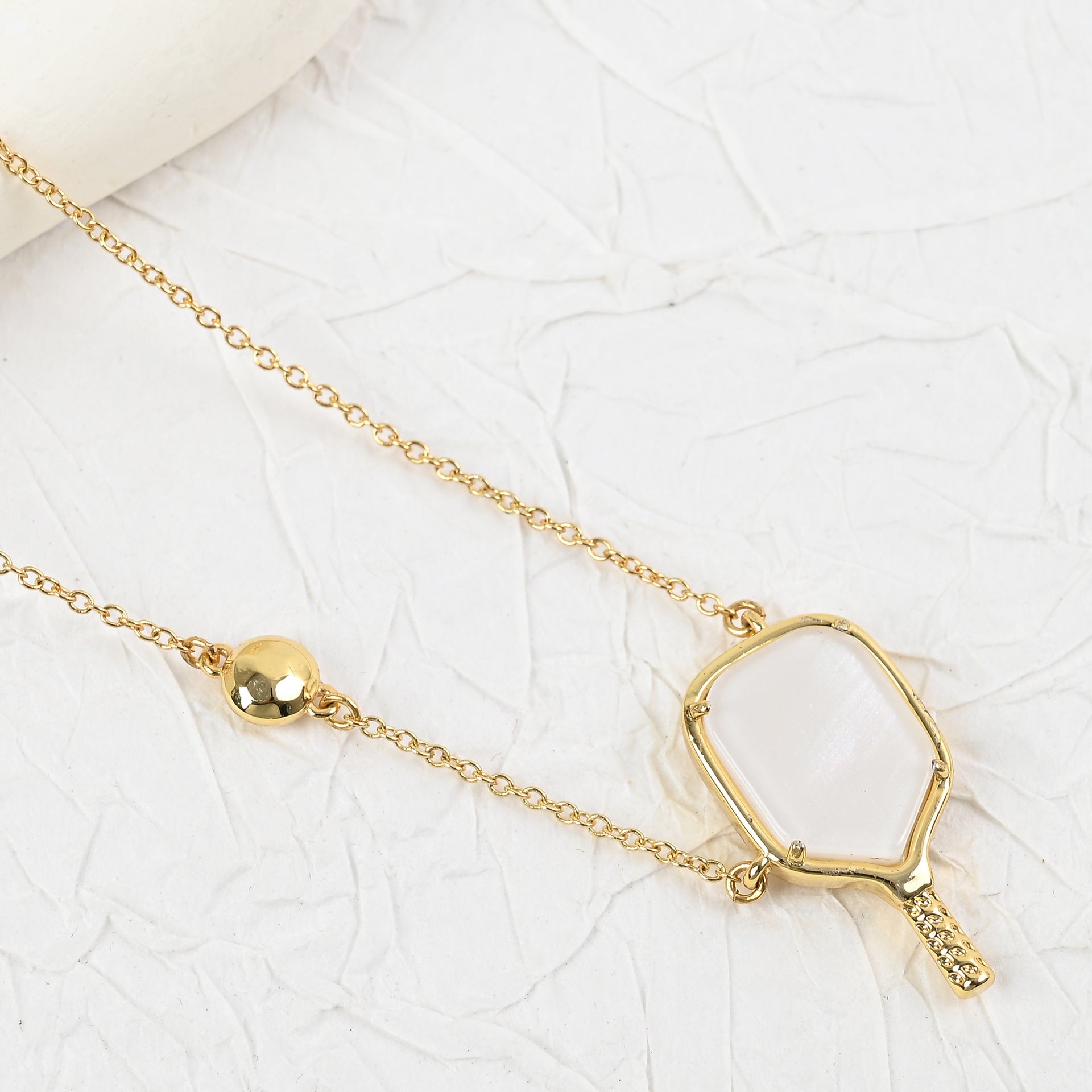 Gold tennis racket pendant necklace with hexagon-framed racket handle detail