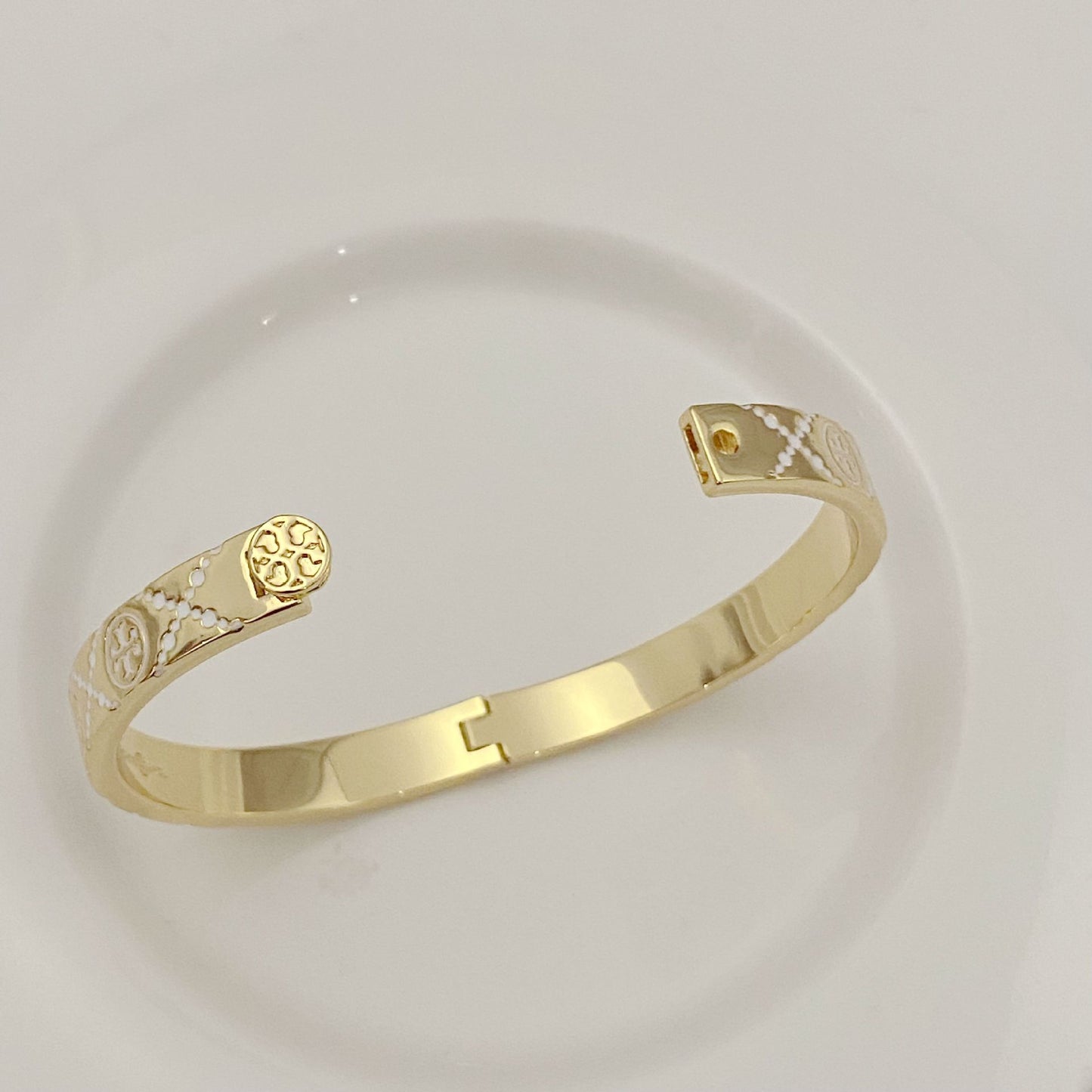 Tory Burch open metal cuff bangle close-up, gold-tone enamel logo at clasp