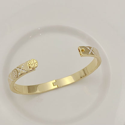 Tory Burch open metal cuff bangle close-up, gold-tone enamel logo at clasp