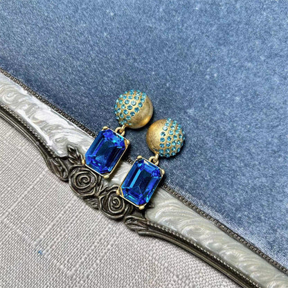 Gold-tone stud earrings with blue square-cut drop stones and round jeweled caps