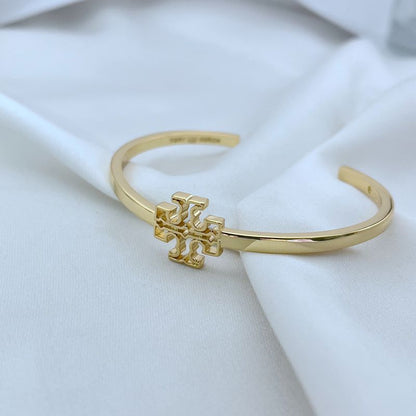Gold tone openwork square logo bangle, side view of smooth cuff and emblem