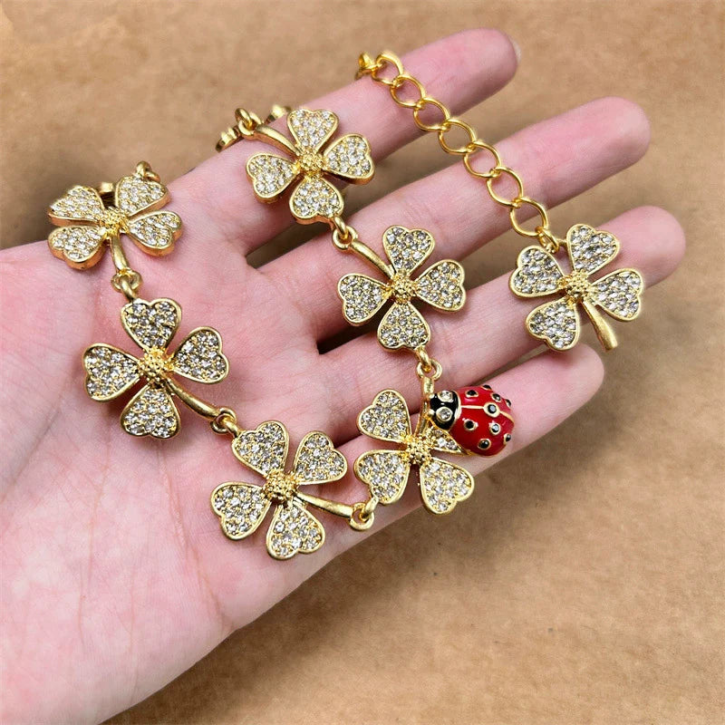 Gold-tone clover crystal necklace with small ladybug bead, held in open hand