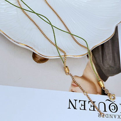 Gold-tone chain necklace with green cord and clasp; red berry charm partially visible