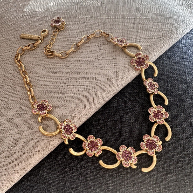 Gold-plated floral pendant necklace with purple rhinestone clover charms and curved links