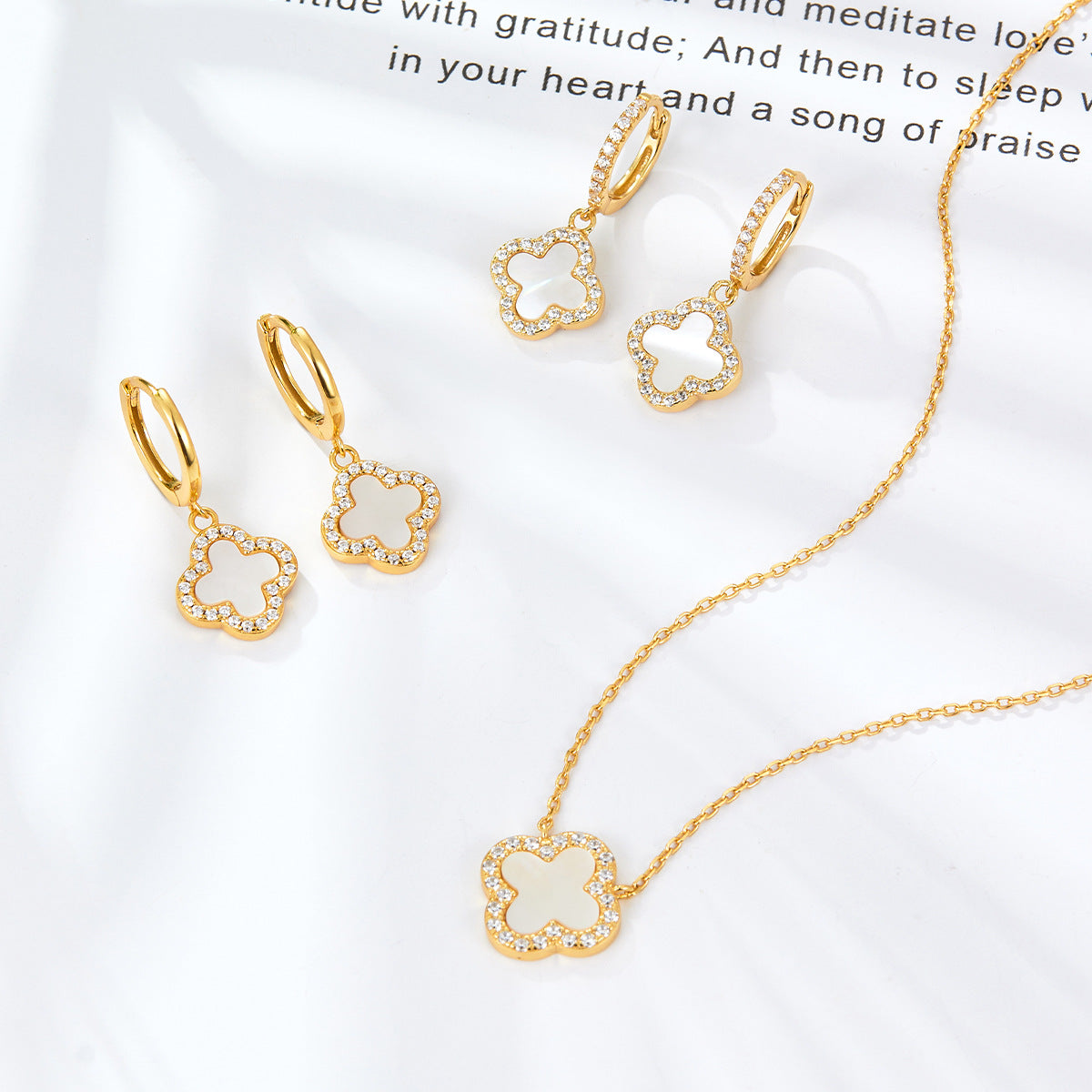 Gold-tone clover hoop earrings with white enamel charm and rhinestone trim