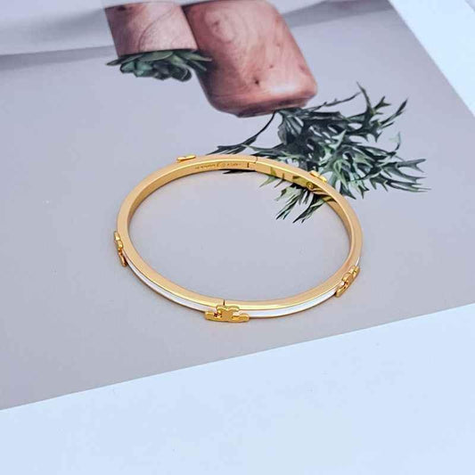 Gold-tone metal bangle with enamel T motif and small link details