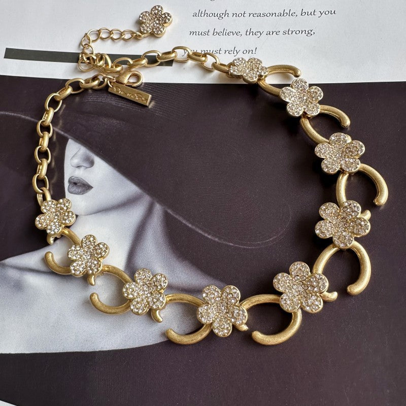 Gold-plated floral pendant necklace with clear rhinestone clover charms and curved links