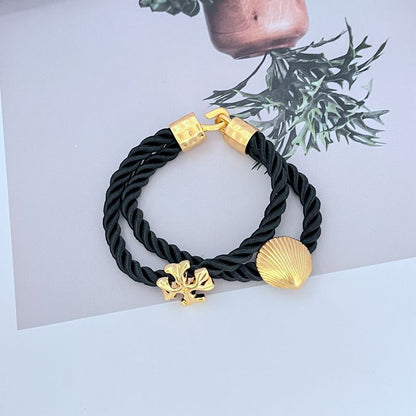 Black braided cord bracelet with gold shell charm and logo toggle clasp