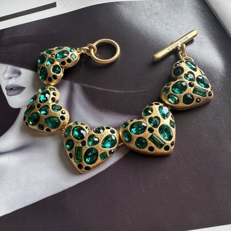 Gold-tone heart charm bracelet with green gemstone accents and toggle bar detail