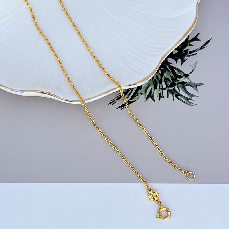Gold metal necklace chain with small logo charm, round clasp detail, stone accents