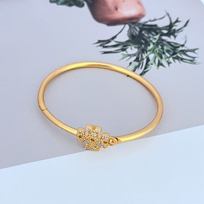 Gold-toned openable bangle with enameled diamond cross centerpiece and hinged clasp