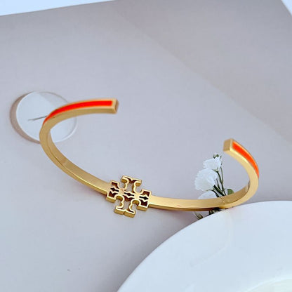 Open gold-tone bangle with cutout logo charm, orange enamel inner edge detail