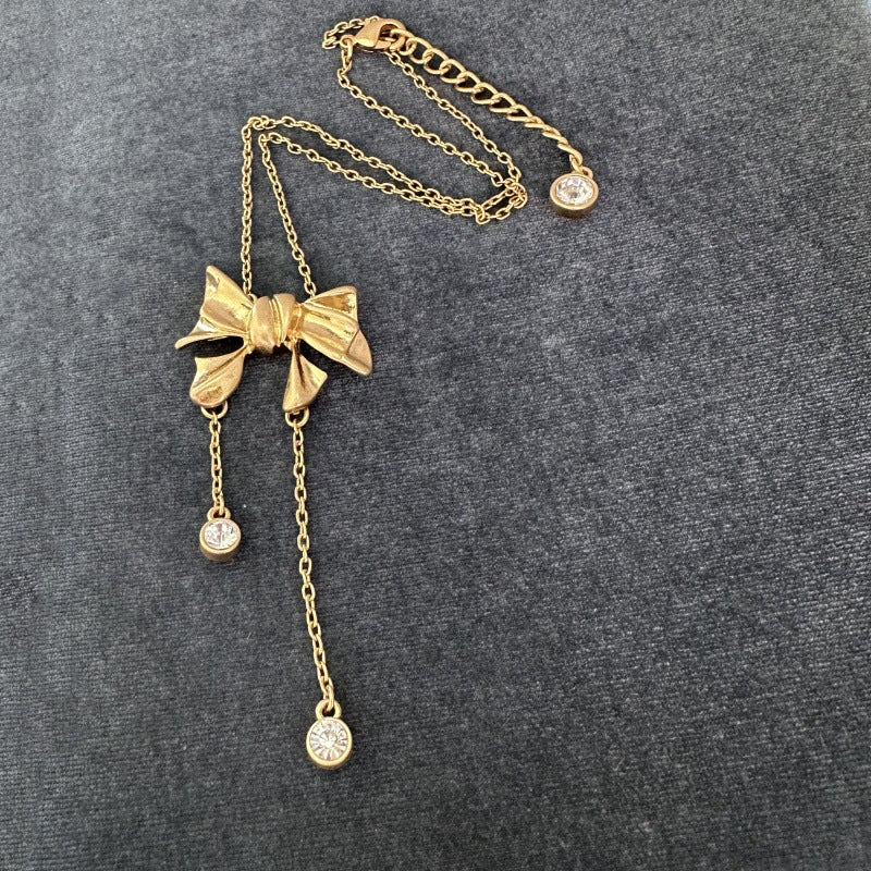 Gold-tone bow necklace with three dangling crystal discs and chain tassel