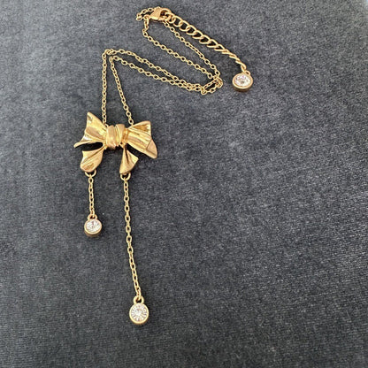 Gold-tone bow necklace with three dangling crystal discs and chain tassel