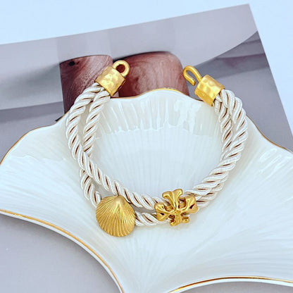 White braided cord bracelet with gold toggle clasp and shell logo centerpiece