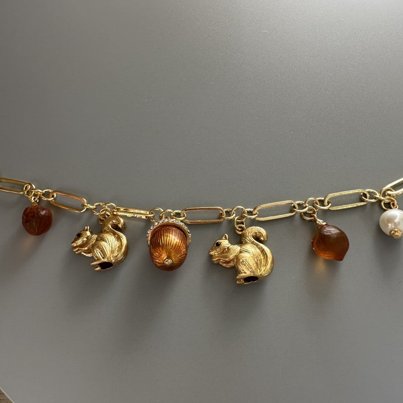 Gold-tone charm bracelet detail with squirrel, acorn, brown drops, and pearl beads