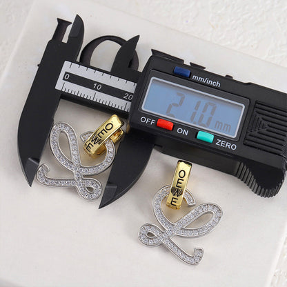 Gold and silver logo stud earrings with openwork outline and clear stones; caliper measurement