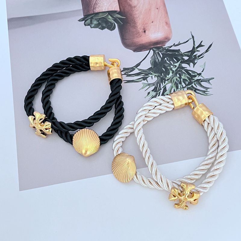 Black and white braided cord bracelets with gold shell charms and logo toggle clasps