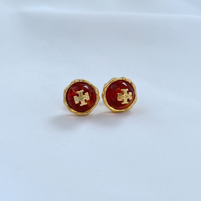 Metal stud earrings with red gemstone and gold logo cross pattern