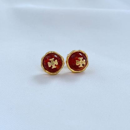 Metal stud earrings with red gemstone and gold logo cross pattern
