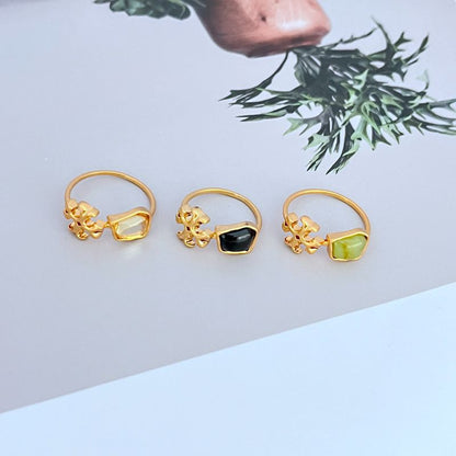 Three logo rings: transparent, black, and green acrylic stones in gold-tone