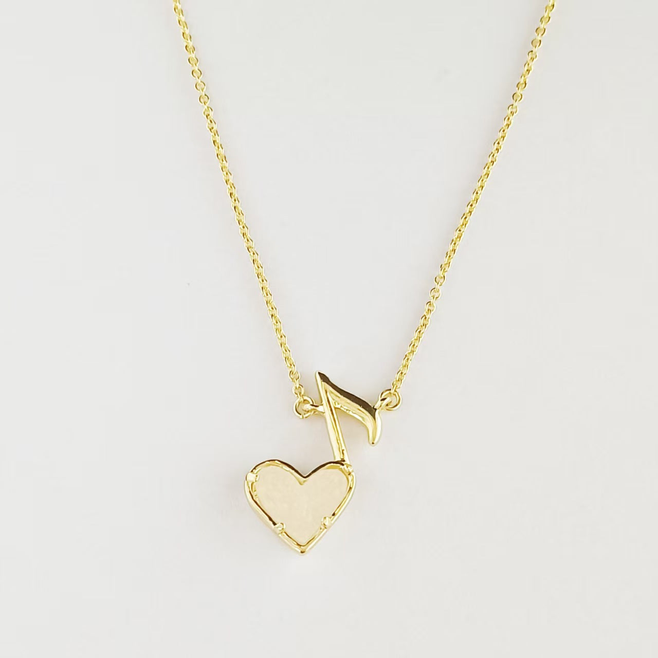 Gold-tone pendant necklace with music note and white heart charm on chain