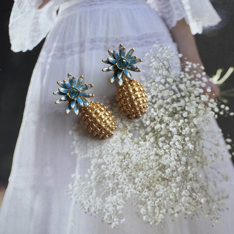 Enamel flower and pineapple diamond earrings with blue flower tops and gold textured drops.