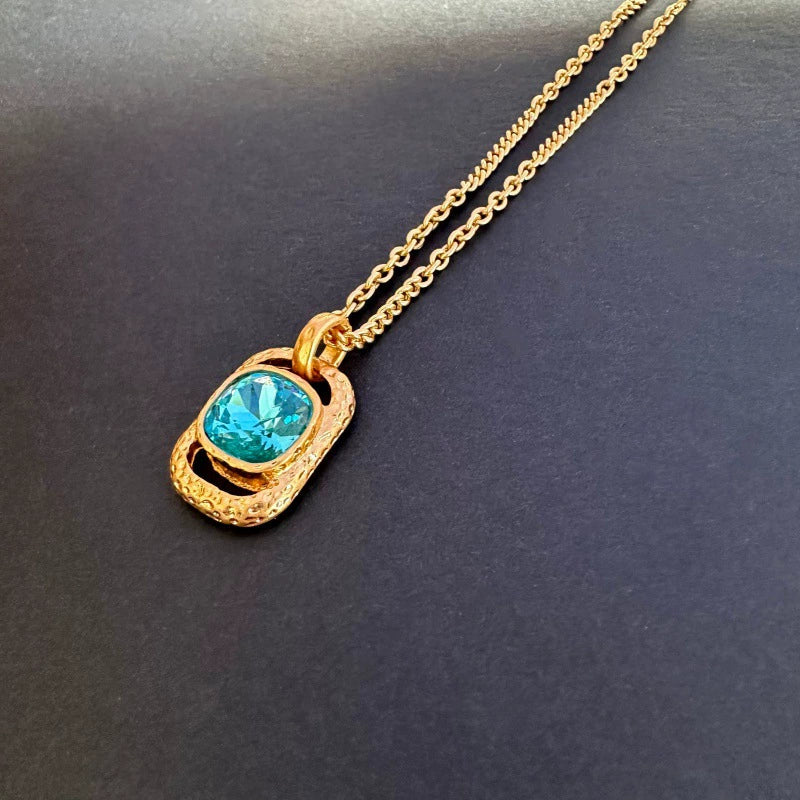 Gold-tone hammered square pendant necklace with turquoise-blue faceted gemstone on chain