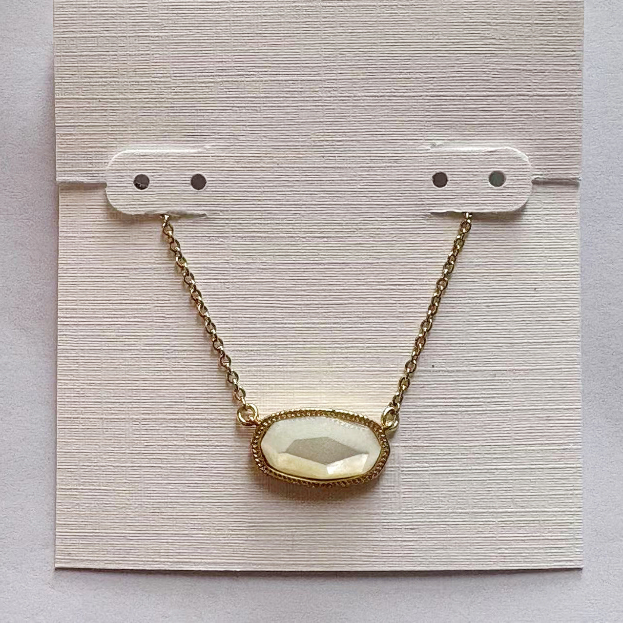 Gold-tone necklace with oval white gemstone pendant displayed on a card backing.