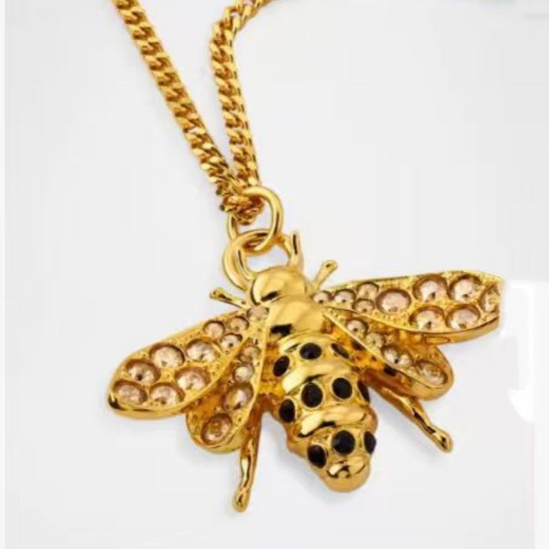 Gold bee pendant necklace with diamond-like wing detailing and black enamel dots
