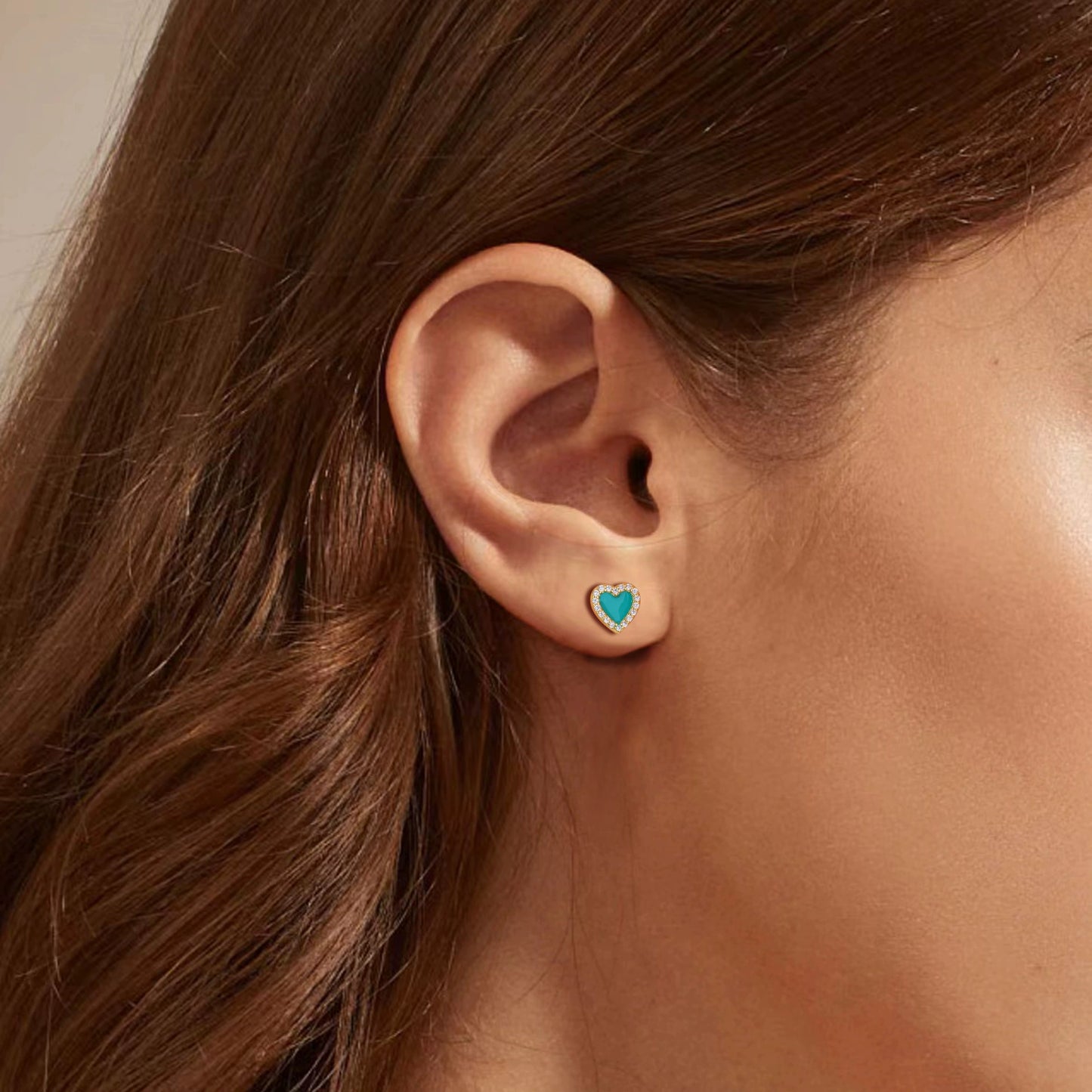 Heart-shaped stud earrings with turquoise enamel and clear stone halo worn on ear.