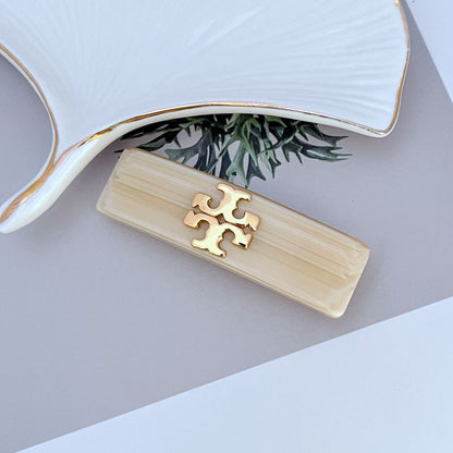 Milky white acrylic logo hair clip with gold interlocking T emblem