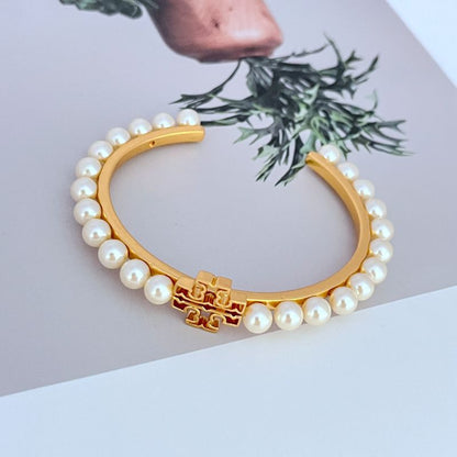 Gold open bangle with white pearl beads and red enamel logo clasp