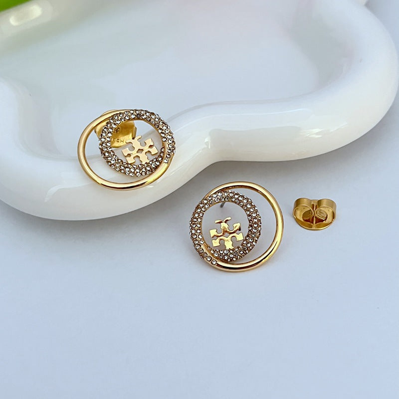 Pair of gold-tone stud earrings, circular frame edged with rhinestones, logo detail