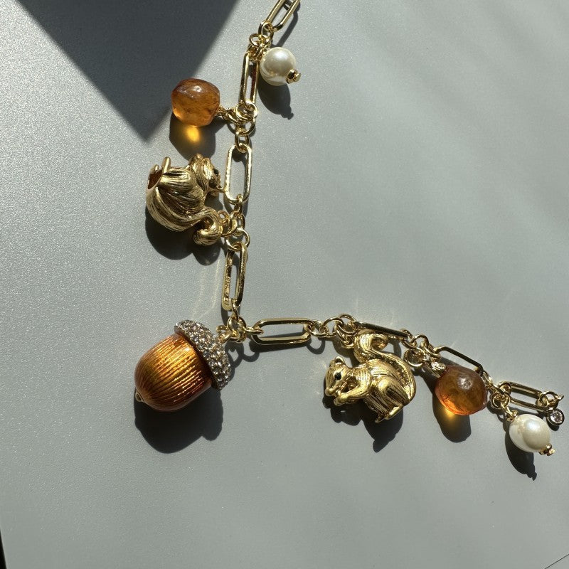 Gold-tone charm bracelet angled view with squirrel, acorn, and pearl drop charms
