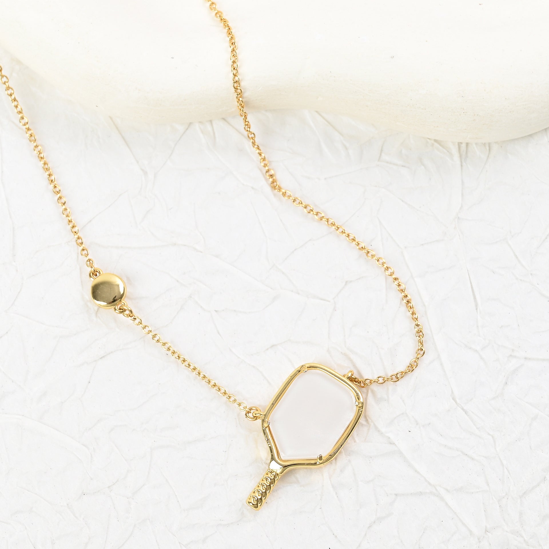 Gold tennis racket pendant necklace with heart-shaped outline and small handle detail