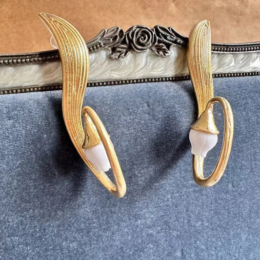 Gold clip-on earrings with white flower dangle accents, oval hoop design