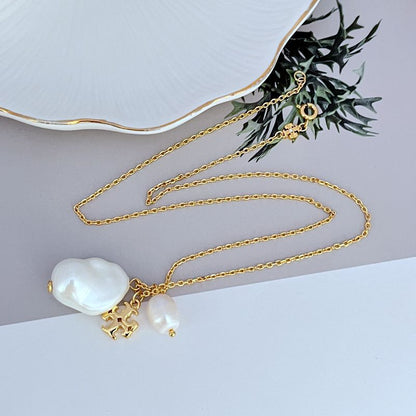 Gold metal necklace with baroque pearl charm and ornate logo pendant, layered chain