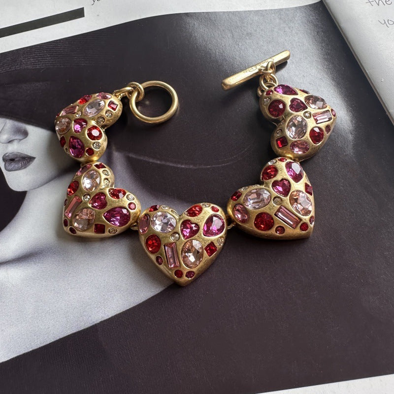 Gold-tone heart charm bracelet with pink gemstone accents and toggle bar detail
