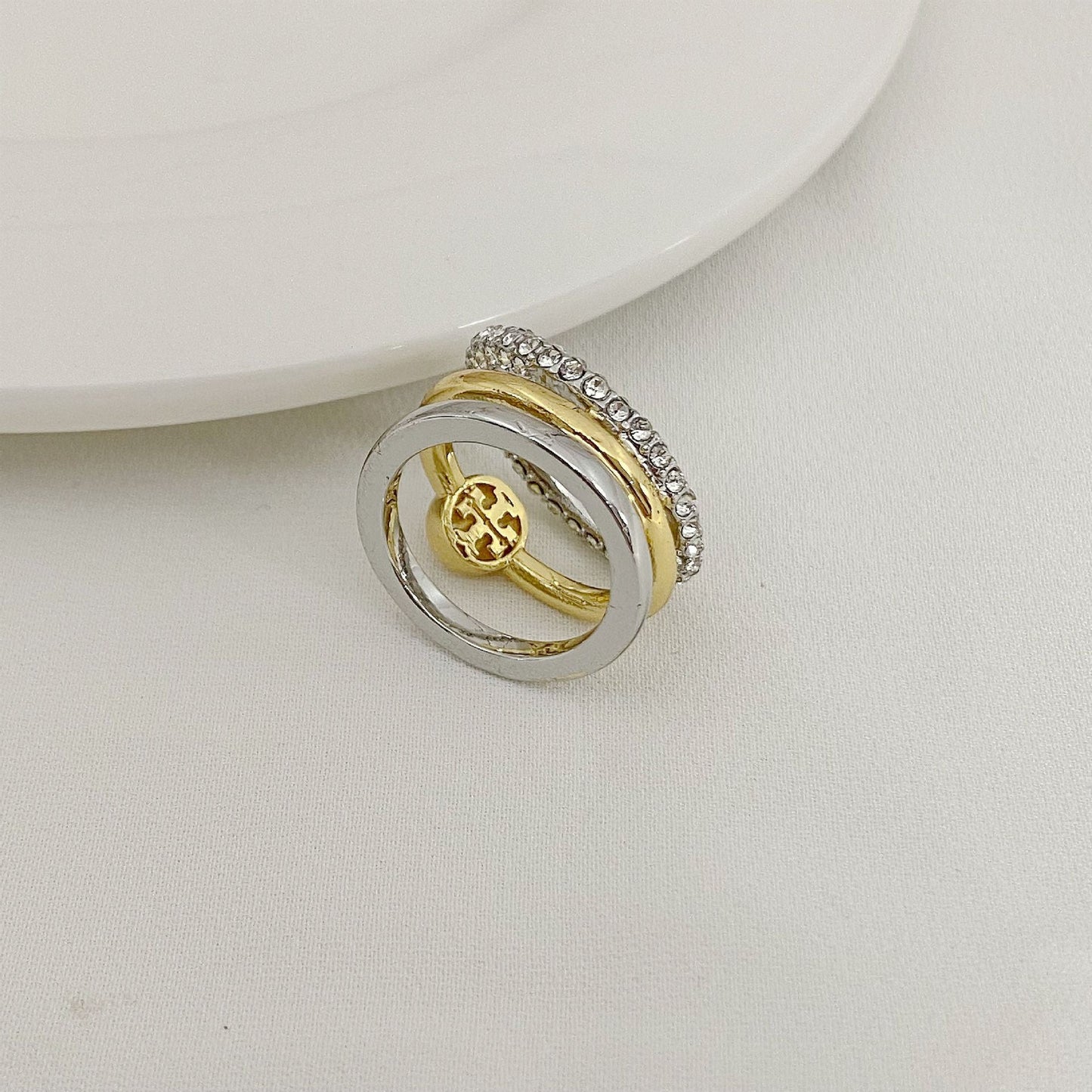 Gold and silver three-band ring with circular logo medallion and rhinestone outer band