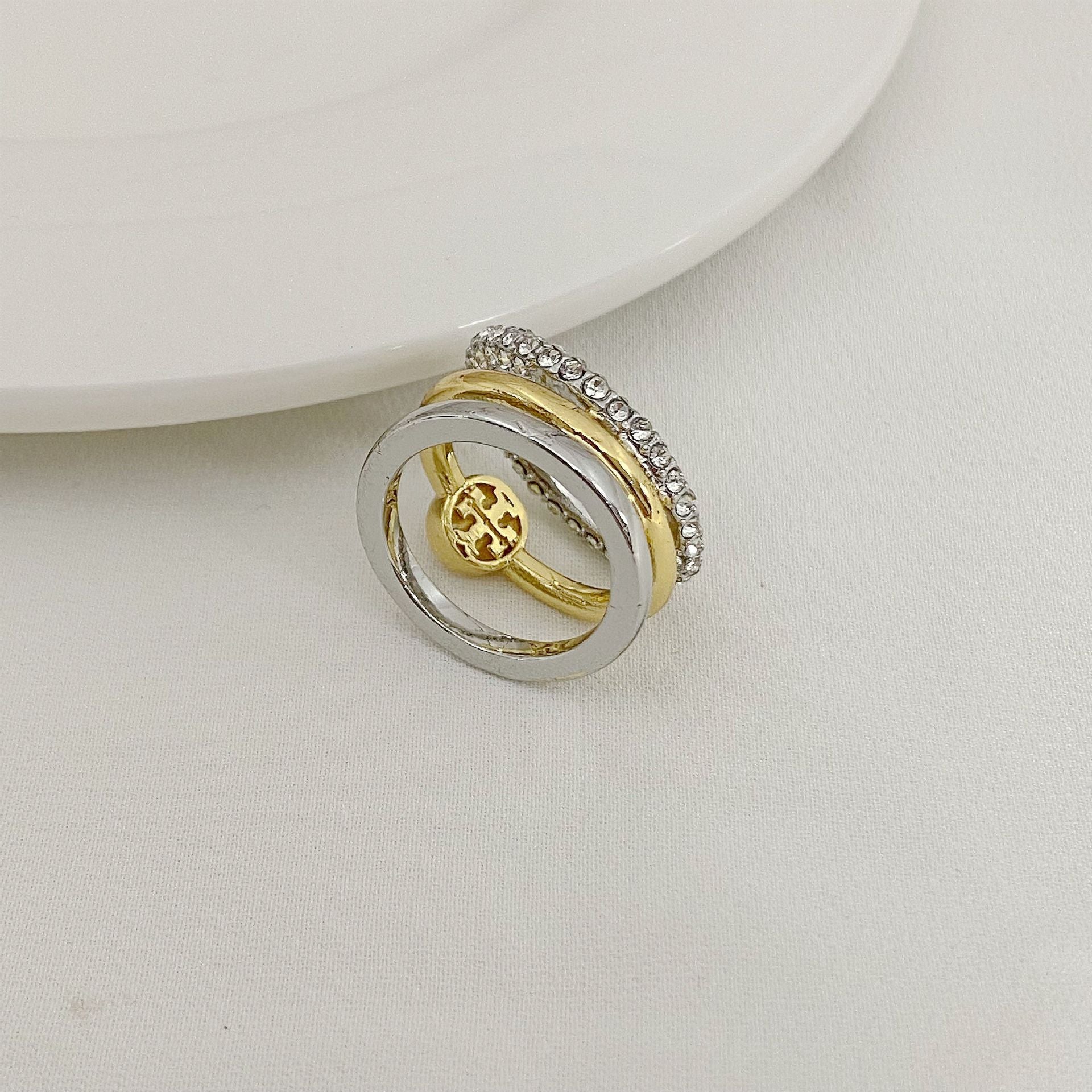 Gold and silver three-band ring with circular logo medallion and rhinestone outer band