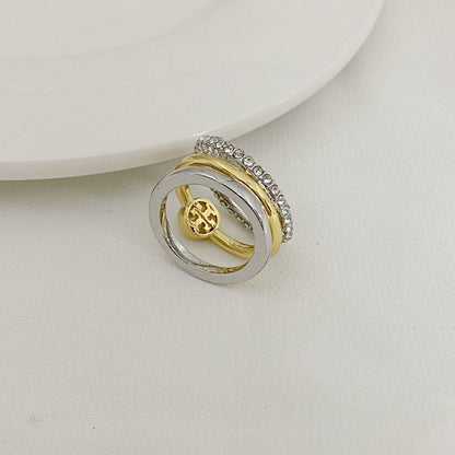 Gold and silver three-band ring with circular logo medallion and rhinestone outer band