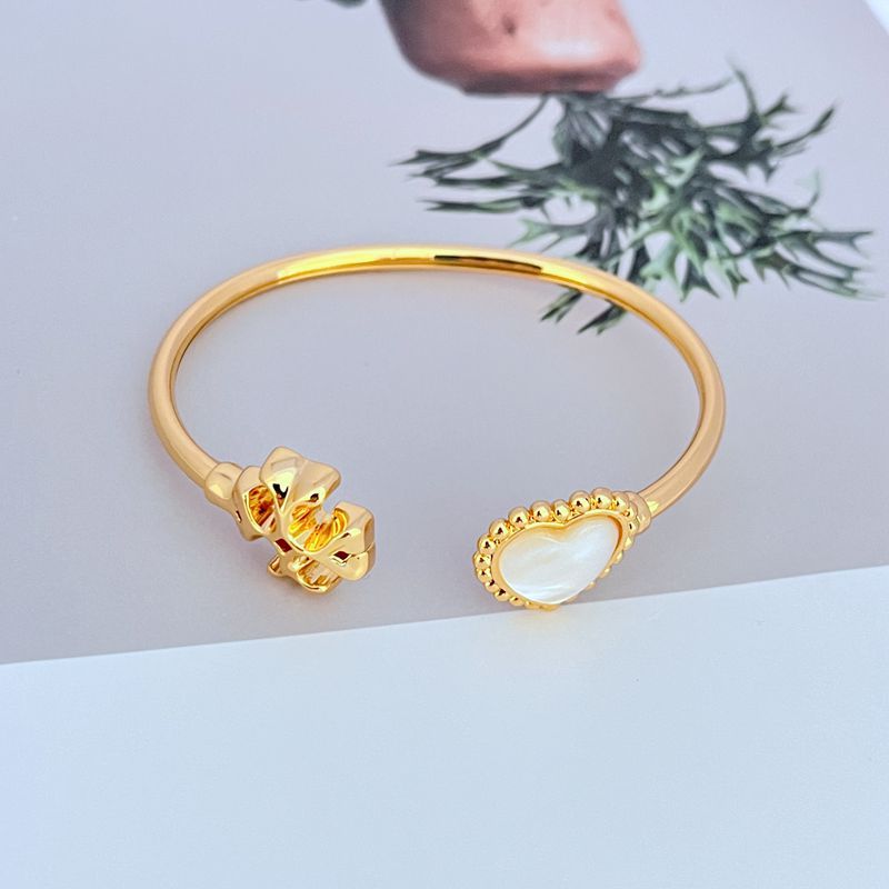 Gold-tone open bangle with heart motif and mother-of-pearl inlay charm