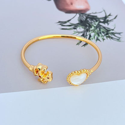 Gold-tone open bangle with heart motif and mother-of-pearl inlay charm