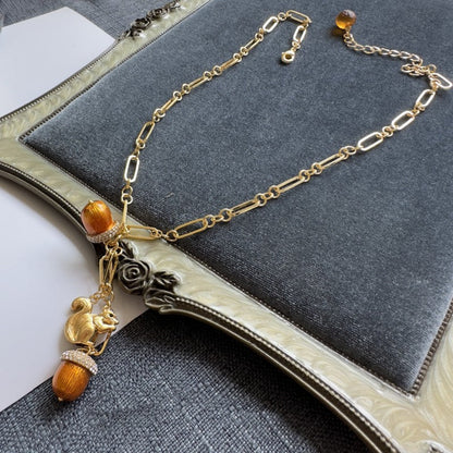 Gold-tone squirrel charm necklace with orange acorn beads and rhinestone caps on chain.