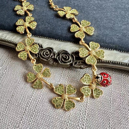 Gold clover crystal necklace detail with ladybug charm and textured chain links