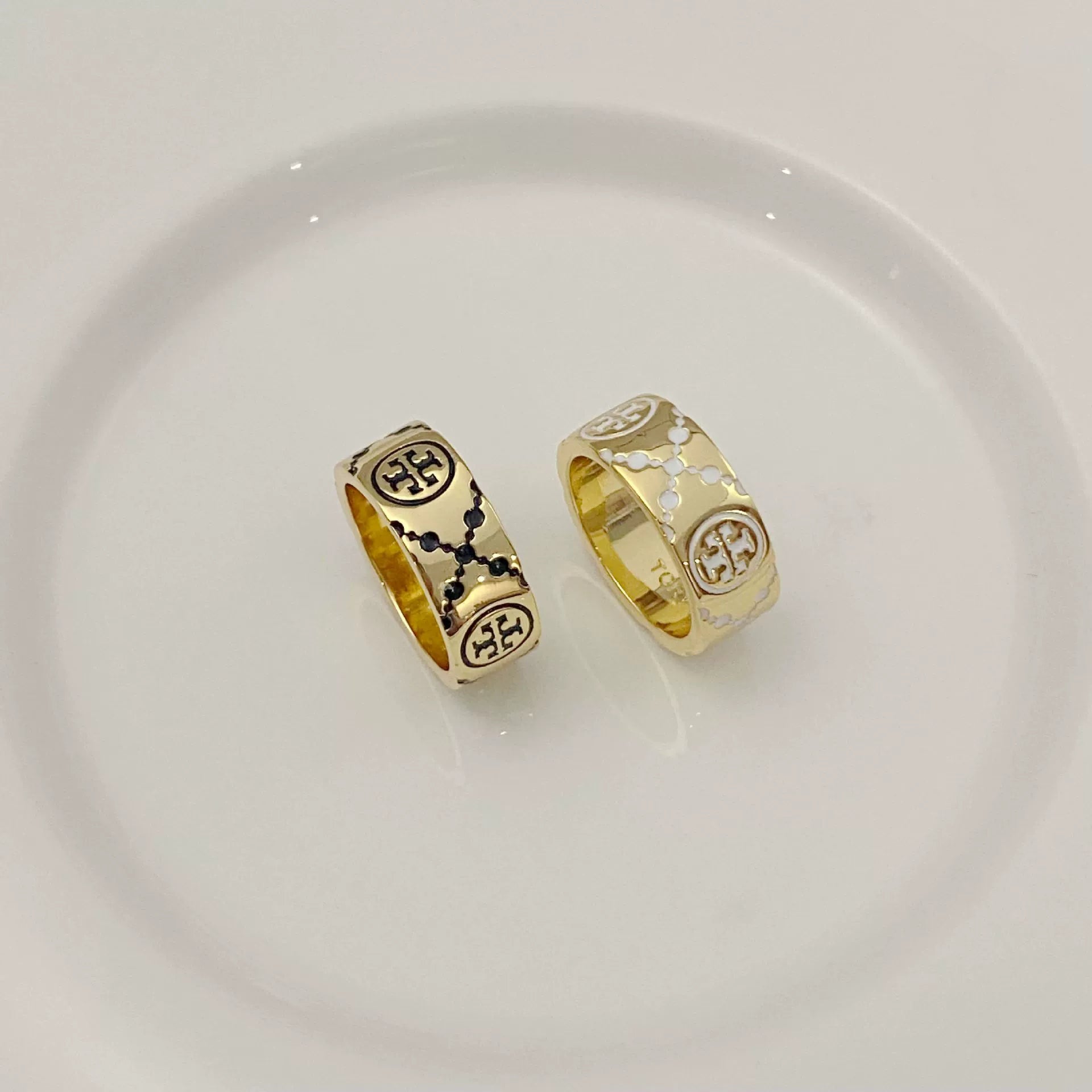 Round logo rings: one dark enamel, one white enamel, gold-tone band