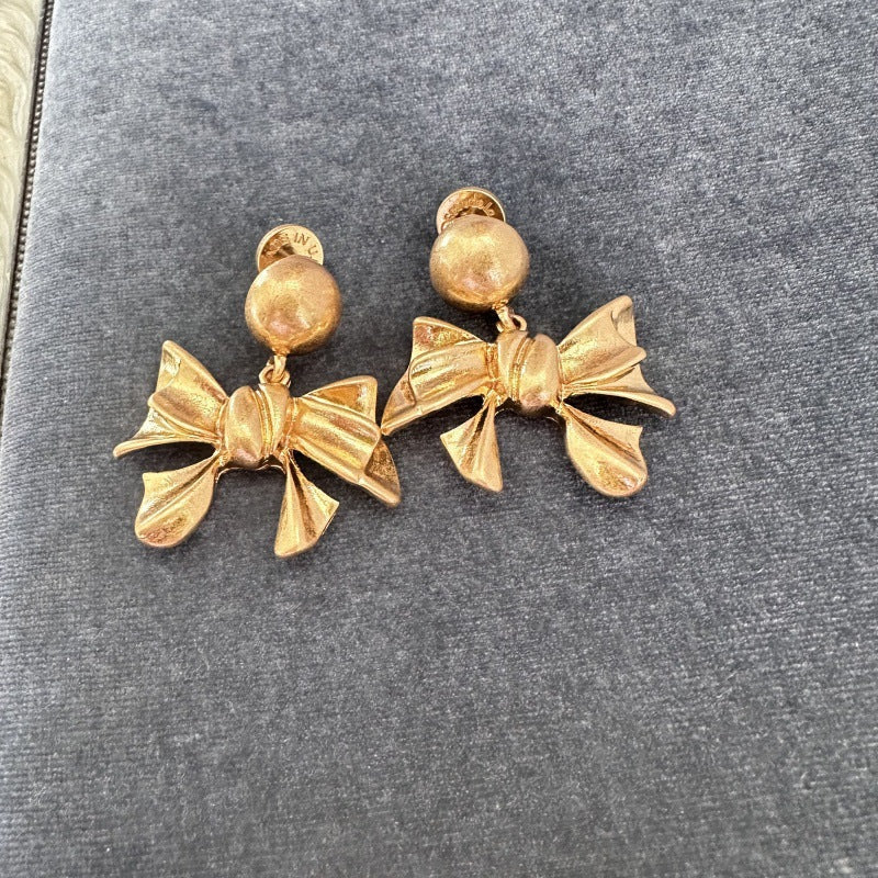 Gold-tone vintage metal bow stud earrings with round top accents and hanging bow drops.